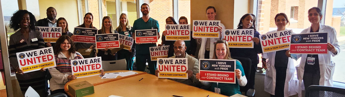 Group photo of PEF members at Helen Hayes Hospital seated and standing in a conference room holding signs that say "We Are United."